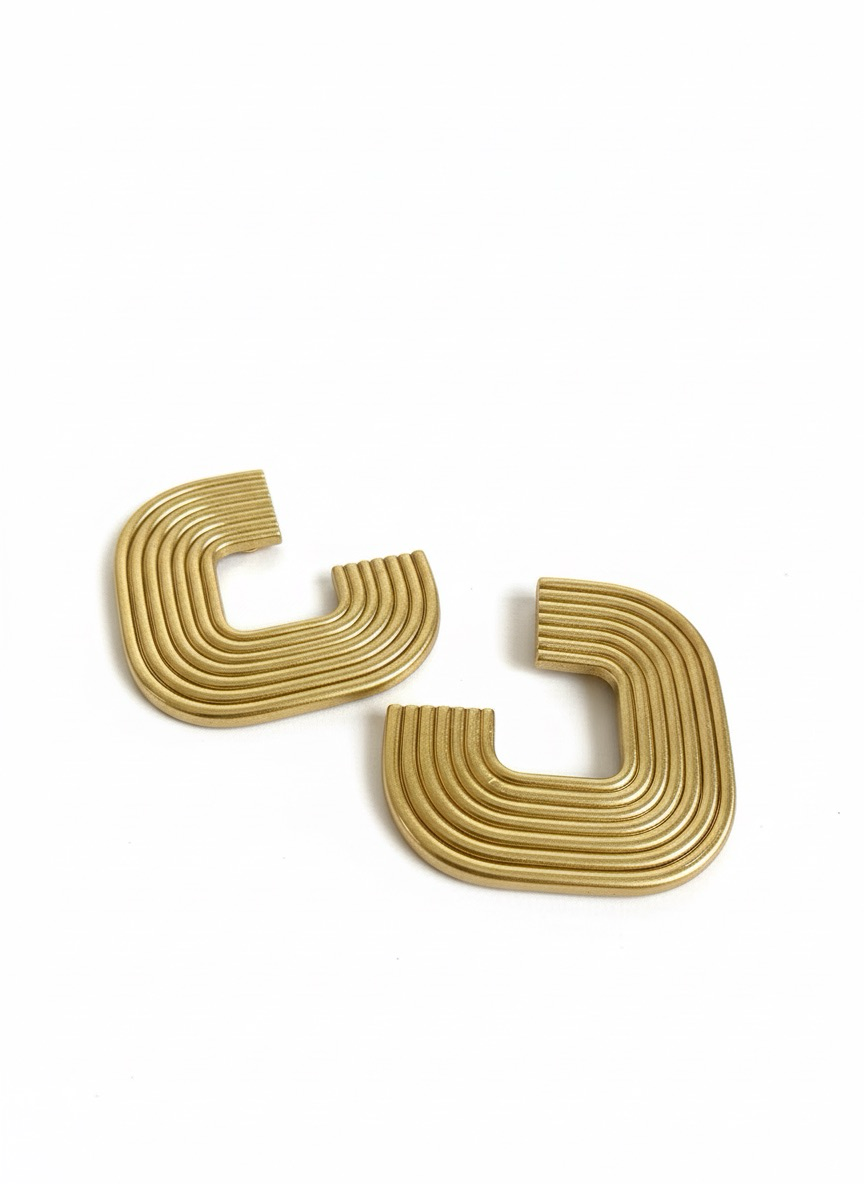 A pair of gold 'Gia' statement earrings on a white surface, handmade by Sunni Dineen.