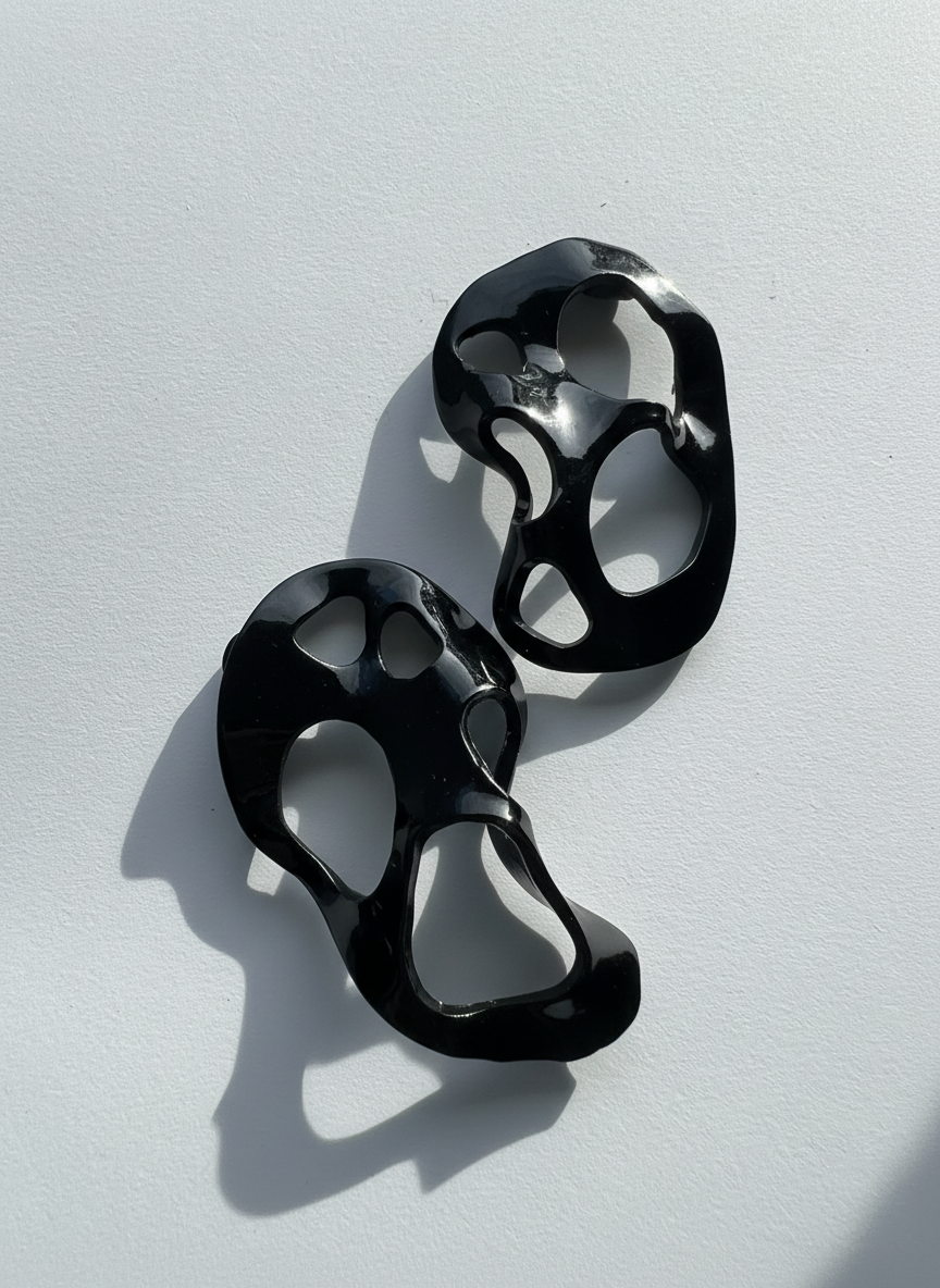 A pair of black 'Alma' sculptural statement earrings displayed on a white surface; handmade by Sunni Dineen.
