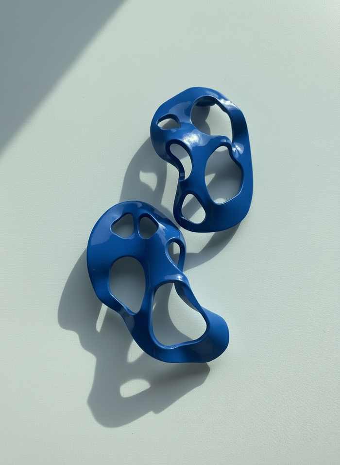 A pair of blue 'Alma' sculptural statement earrings displayed on a white surface; handmade by Sunni Dineen.