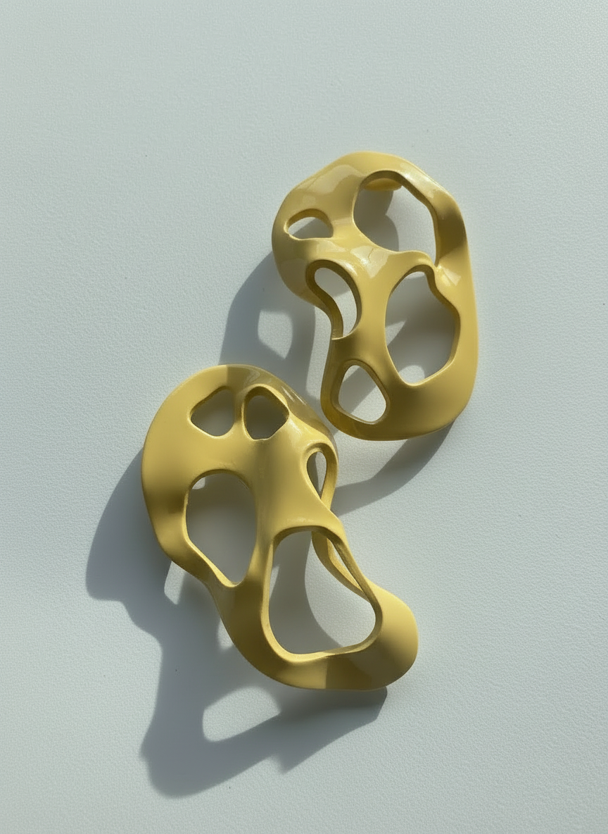 A pair of buttercream yellow 'Alma' sculptural statement earrings displayed on a white surface; handmade by Sunni Dineen.