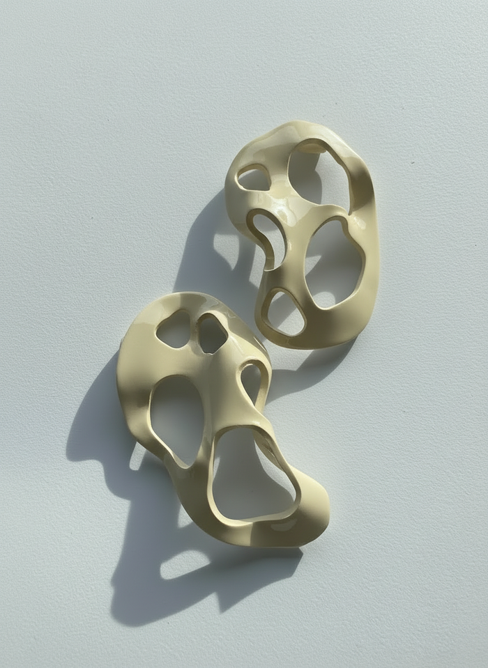 A pair of cream 'Alma' sculptural statement earrings displayed on a white surface; handmade by Sunni Dineen.