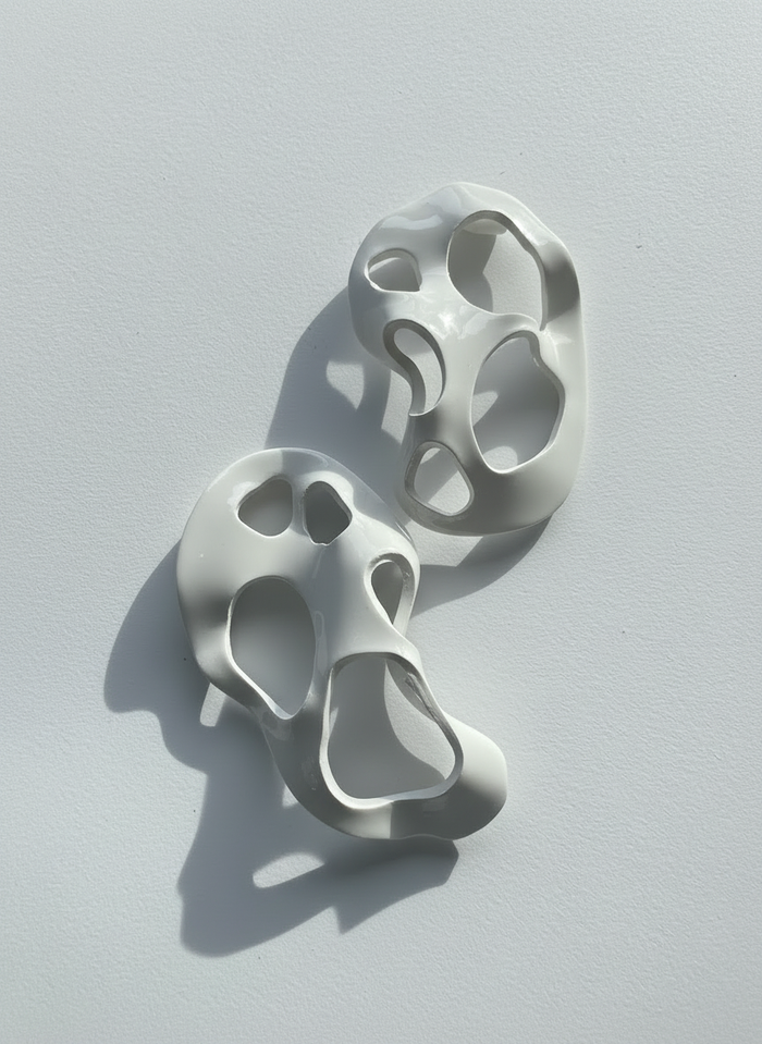 A pair of white 'Alma' sculptural statement earrings displayed on a white surface; handmade by Sunni Dineen.