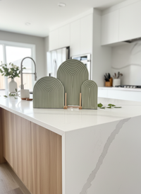 Sage colored arch trays in small, medium and large sizes handmade by Sunni Dineen, displayed and stacked standing up on a modern marble and wood kitchen island.