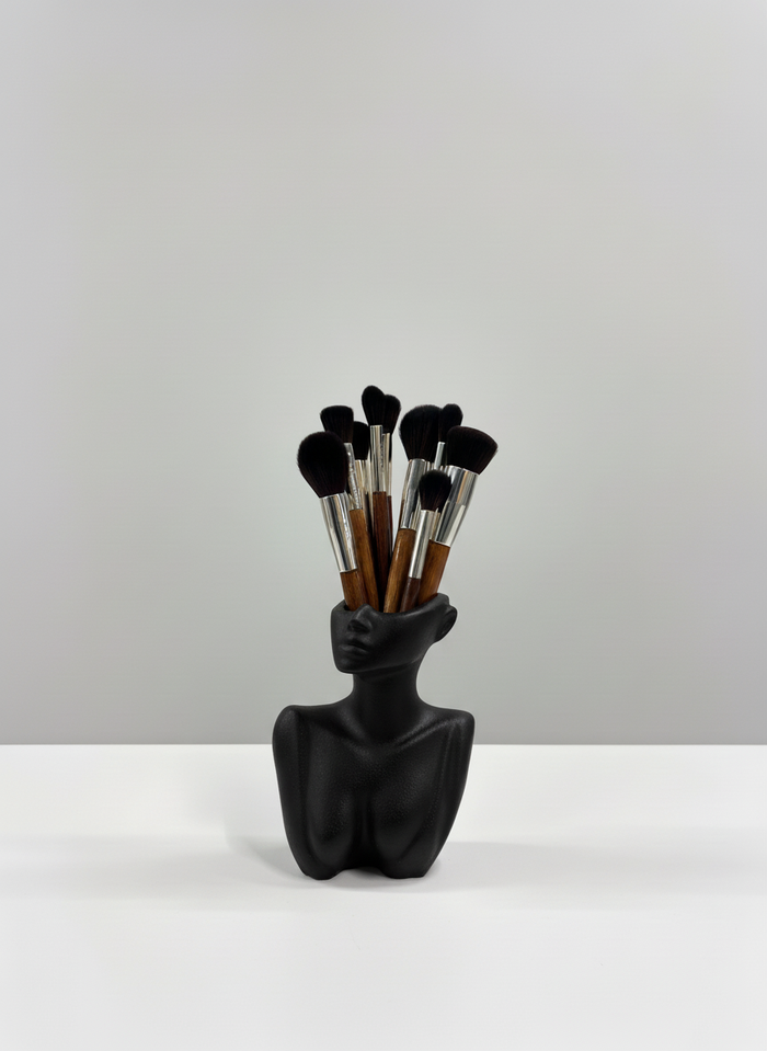The Handcrafted Décolletage Vase made by Sunni Dineen, in black color, displayed holding makeup brushes on a white surface and neutral background.