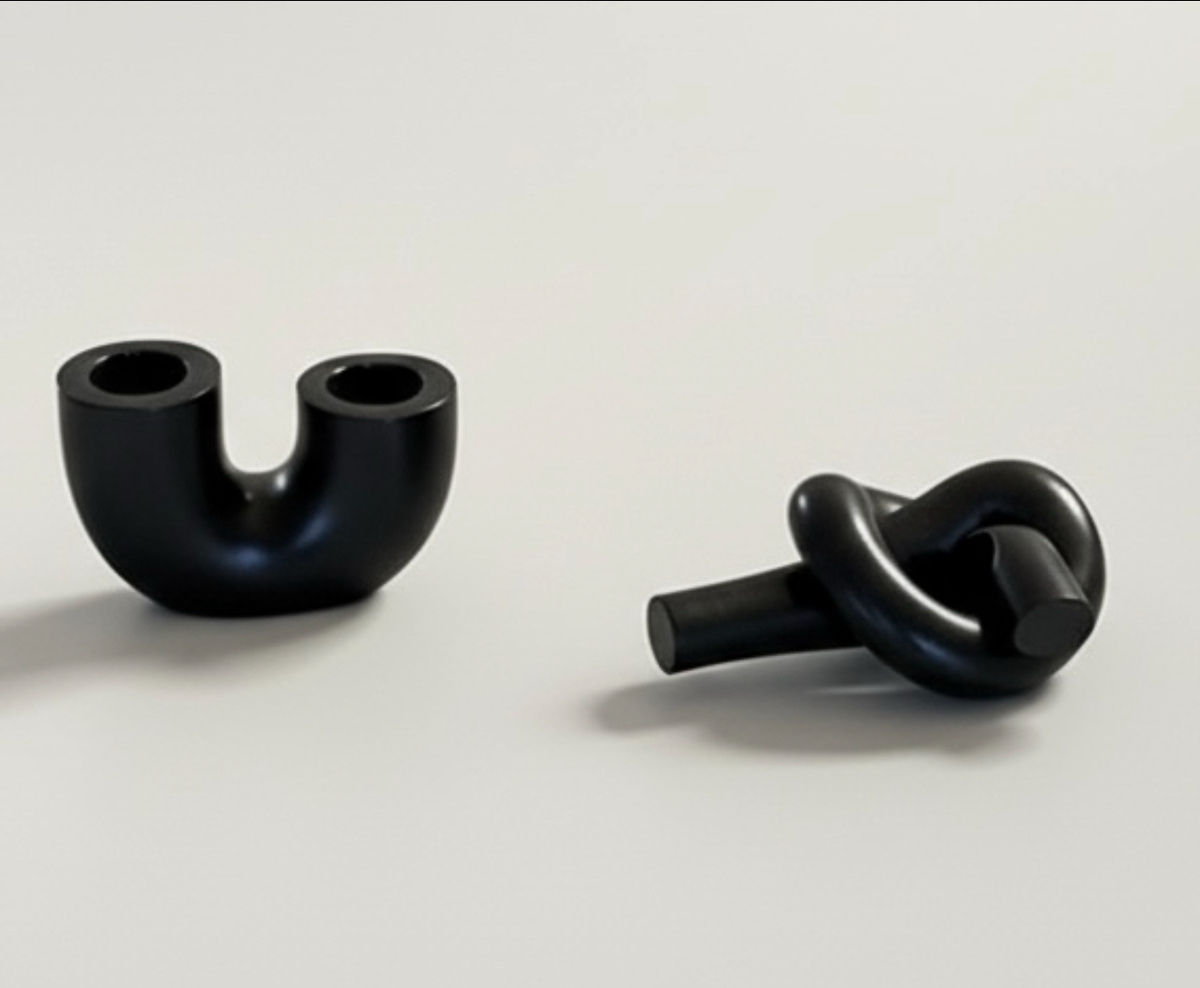 A black U-shaped candlestick holder & black knot candlestick holder handmade by Sunni Dineen, displayed on a white surface.