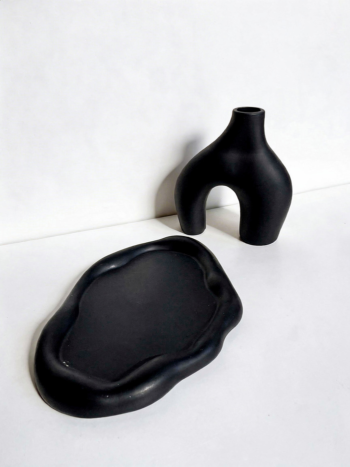 A black-colored Cloud Trinket Dish and blacked-colored Modern Sculptural Horseshoe Vase on a white surface.