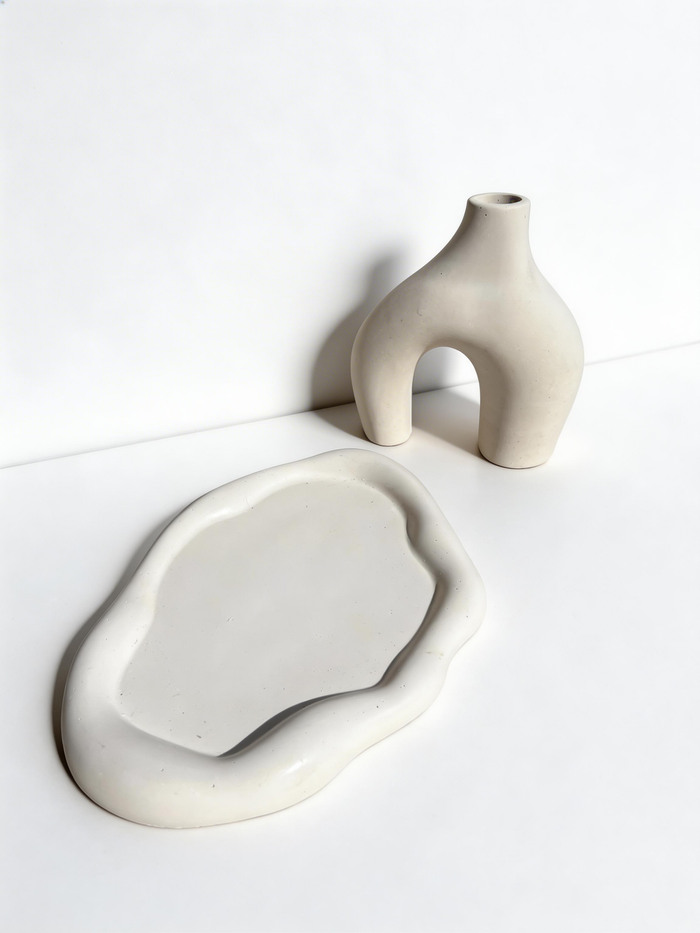 A bone-colored Cloud Trinket Dish and bone-colored Modern Sculptural Horseshoe Vase on a white surface.