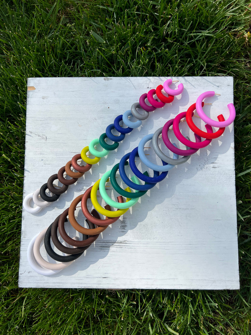 Classic Signature Clay Hoop Earrings of various sizes and colors, handmade by Sunni Dineen, displayed on white surface with green grassy background.