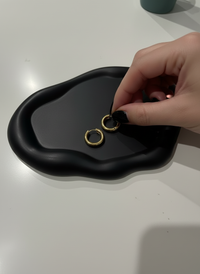 Gold hoop earrings being held over a black cloud trinket dish handmade by Sunni Dineen.