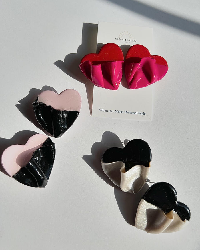 The Draped Heart Statement Earrings in all color variants displayed on a white surface, handmade by Sunni Dineen.