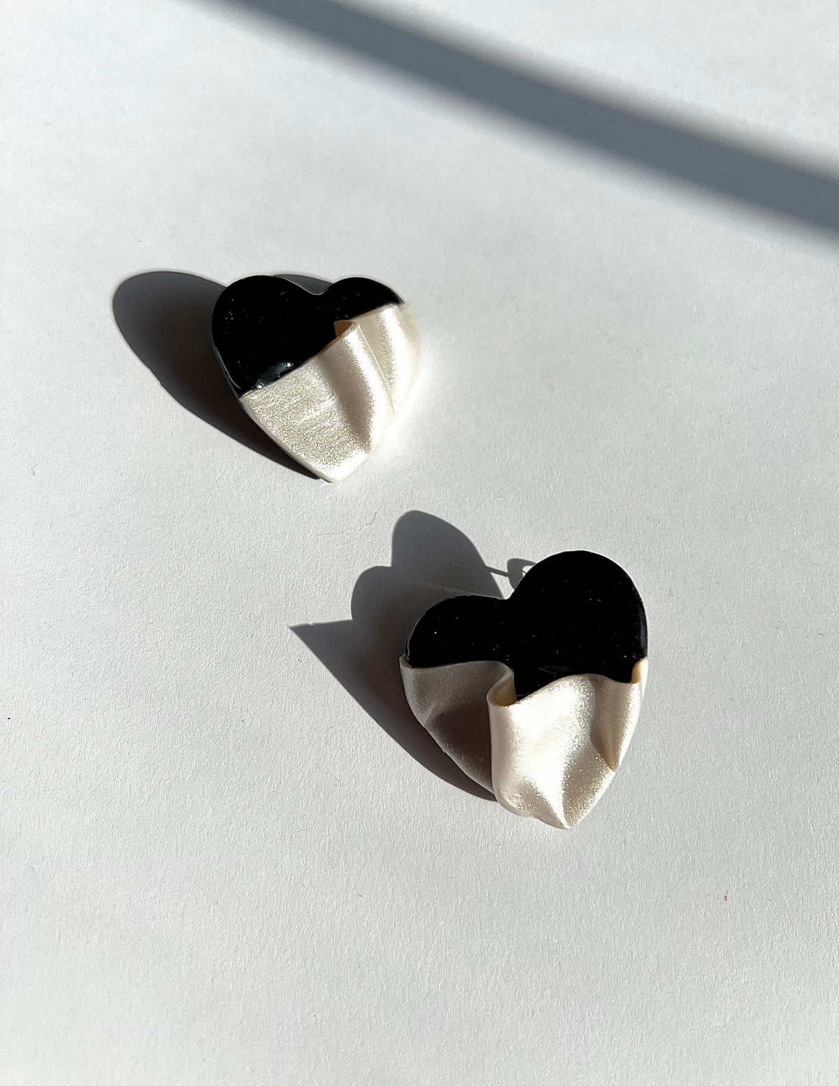 The Draped Heart Statement Earrings in black-pearl displayed on a white surface, handmade by Sunni Dineen.
