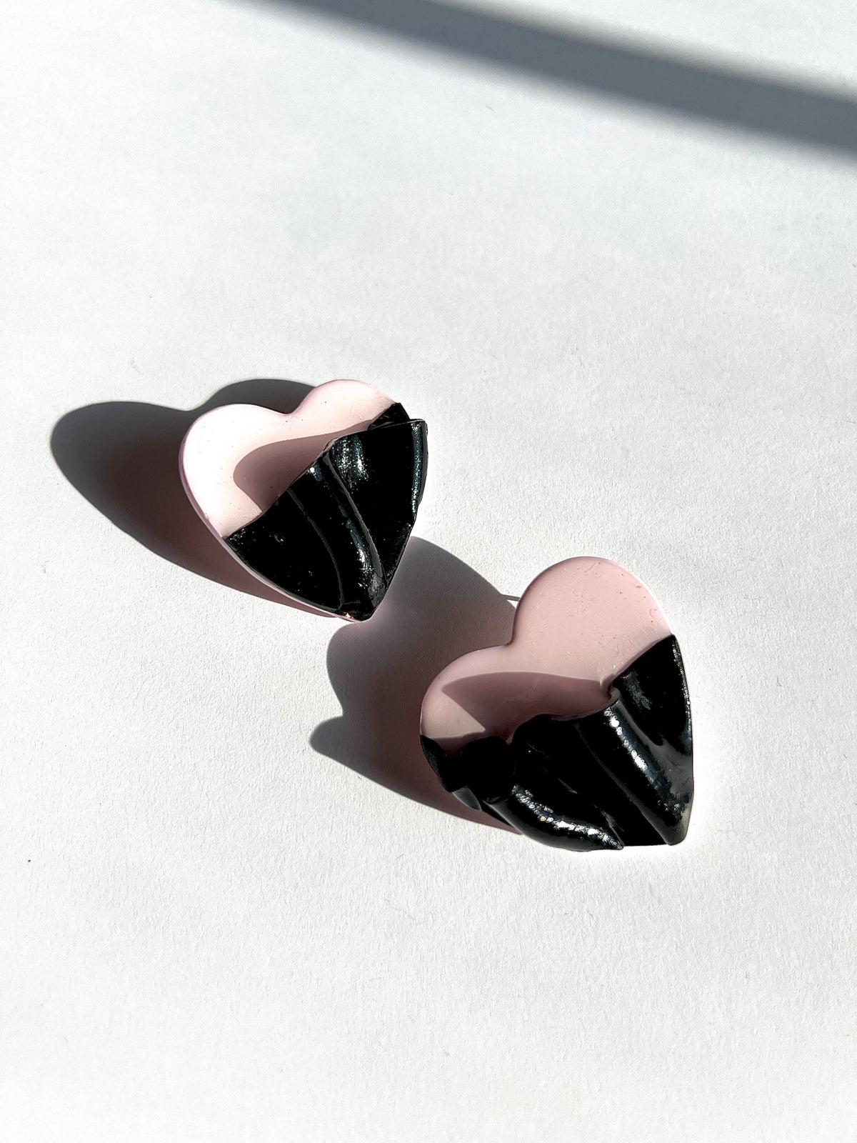 The Draped Heart Statement Earrings in pink-black displayed on a white surface, handmade by Sunni Dineen.