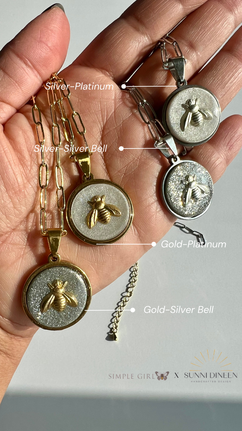 Hand holding four Queen Honeybee Pendant Necklaces with color variation labels from SGB X SDHD Collection.