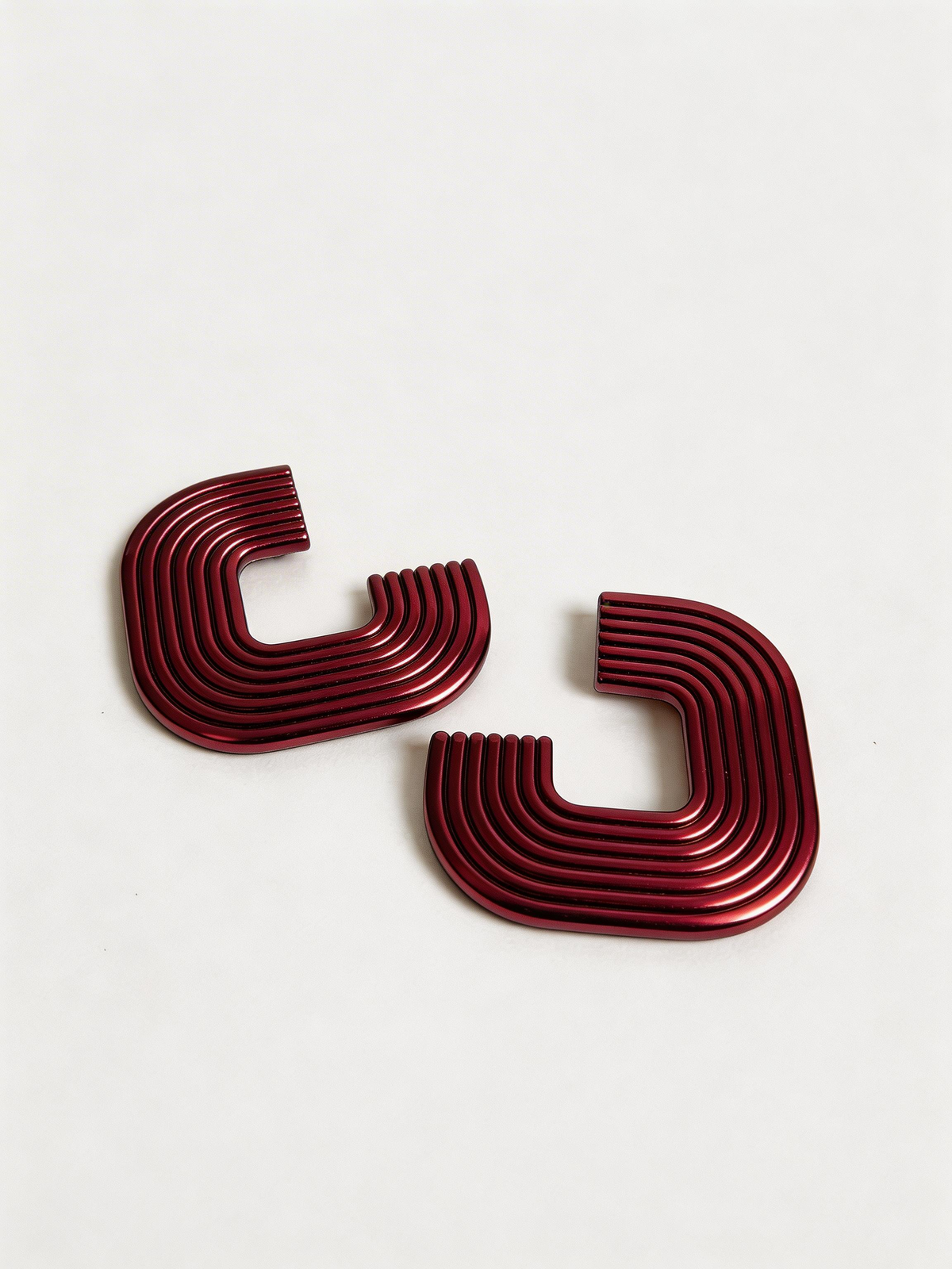 A pair of metallic cranberry 'Gia' statement earrings on a white surface, handmade by Sunni Dineen.