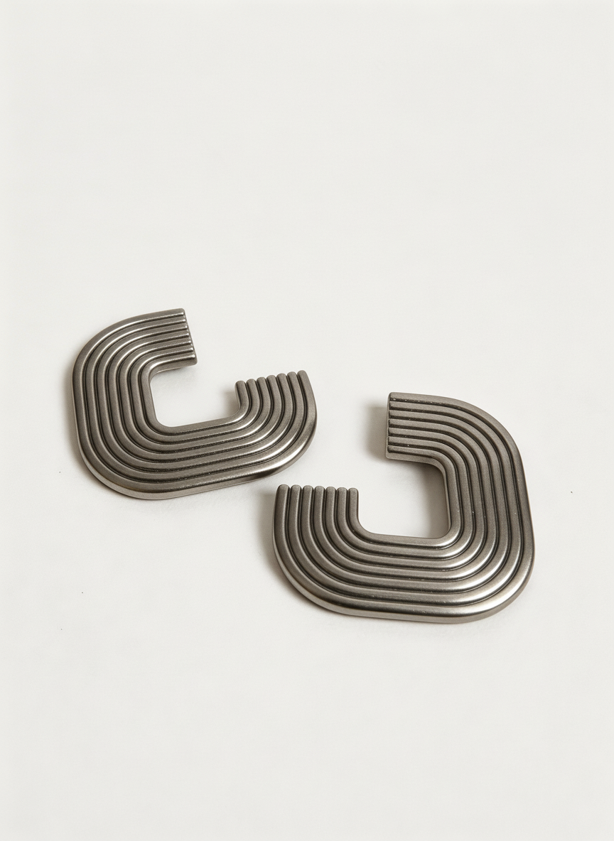 A pair of silver 'Gia' statement earrings on a white surface, handmade by Sunni Dineen.