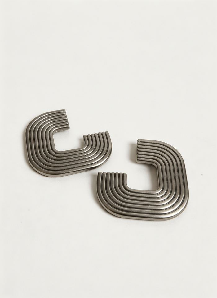 A pair of silver 'Gia' statement earrings on a white surface, handmade by Sunni Dineen.