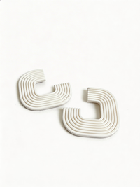A pair of white 'Gia' statement earrings on a white surface, handmade by Sunni Dineen.