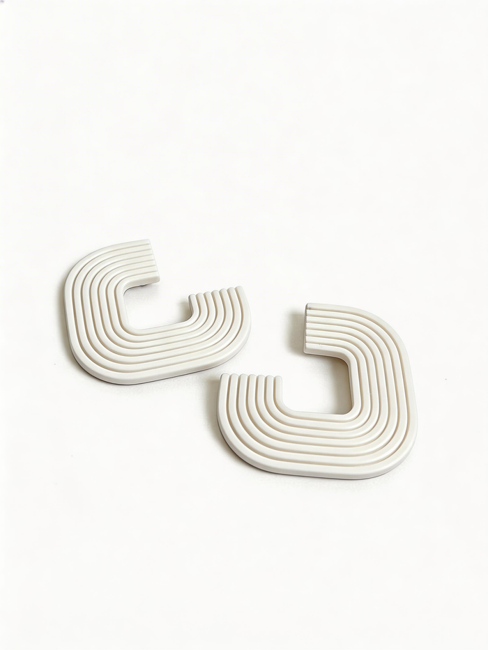 A pair of white 'Gia' statement earrings on a white surface, handmade by Sunni Dineen.