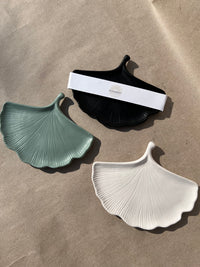 Three Ginkgo Leaf Trinket Dishes in black, sage, and white; handmade by Sunni Dineen; arranged on a kraft paper surface.