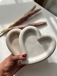 Sunni Dineen's hand holding two trinket dishes over a neutral white surface with dry pampas lying on the surface.