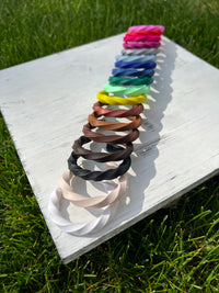 Colorful collection of "Helix Clay Hoop Earrings' arranged on a white wooden board with grass in the background.