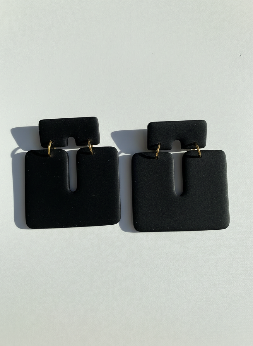 Pair of black 'Kalani' statement earrings, handmade by Sunni Dineen, on a white textured surface.