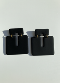 Pair of black 'Kalani' statement earrings, handmade by Sunni Dineen, on a white textured surface.