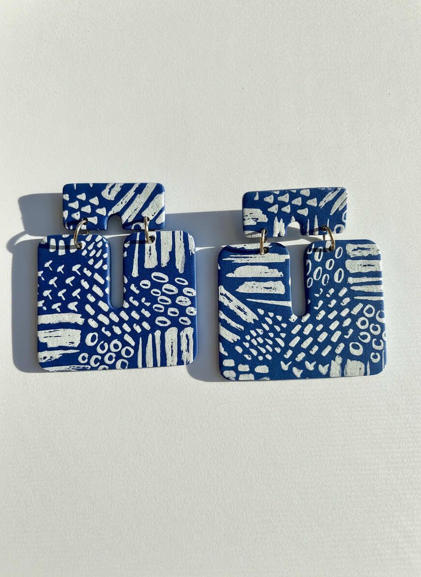 Pair of blue and white patterned 'Kalani' statement earrings, handmade by Sunni Dineen, on a white textured surface.