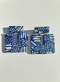 Pair of blue and white patterned 'Kalani' statement earrings, handmade by Sunni Dineen, on a white textured surface.