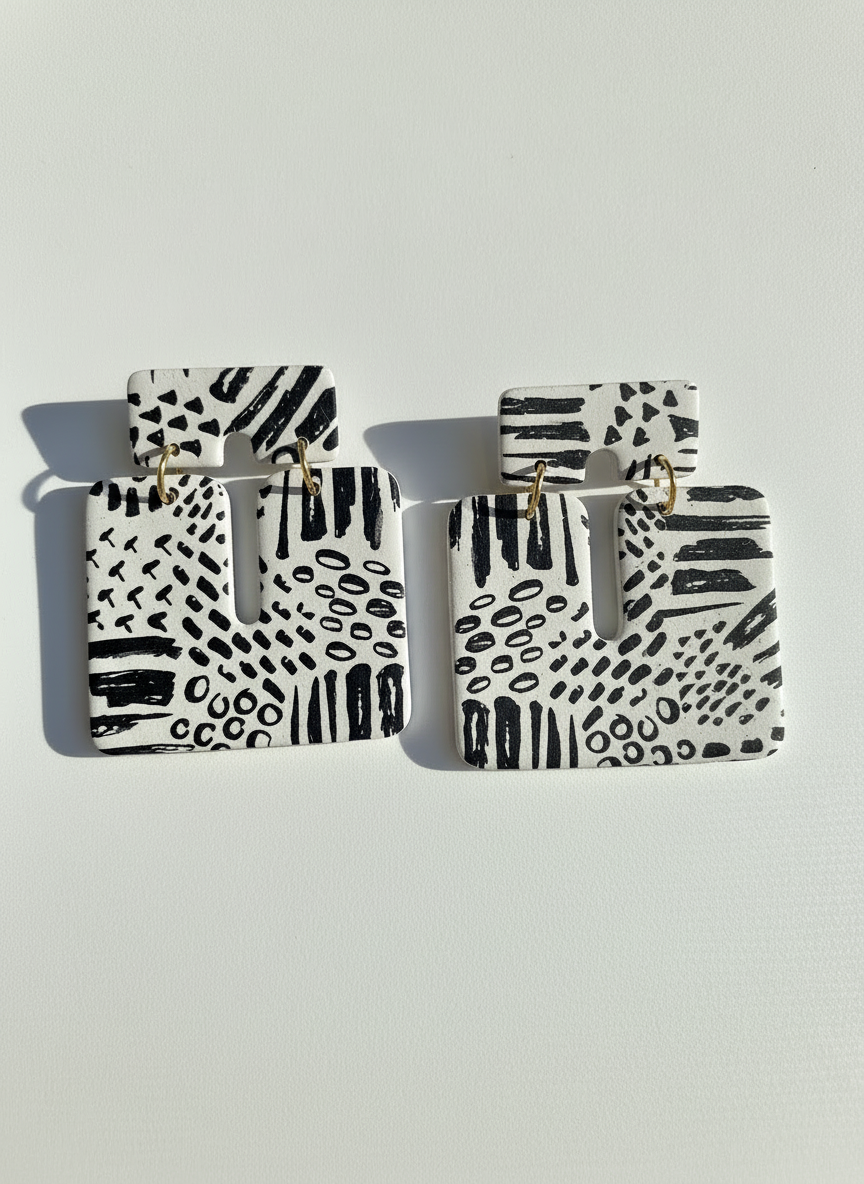 Pair of white and black patterned 'Kalani' statement earrings, handmade by Sunni Dineen, on a white textured surface.
