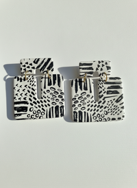 Pair of white and black patterned 'Kalani' statement earrings, handmade by Sunni Dineen, on a white textured surface.