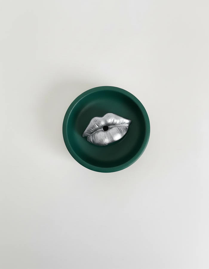 A green Sculptural Lips Incense Holder with silver lips, handmade by Sunni Dineen, displayed on a white surface.
