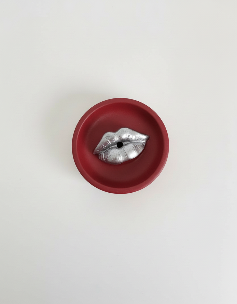 A red Sculptural Lips Incense Holder with silver lips, handmade by Sunni Dineen, displayed on a white surface.