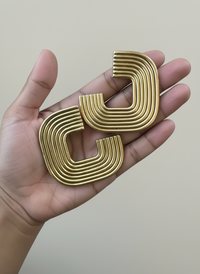 Hand holding the a pair of gold Gia Statement Earrings, handmade by Sunni Dineen.