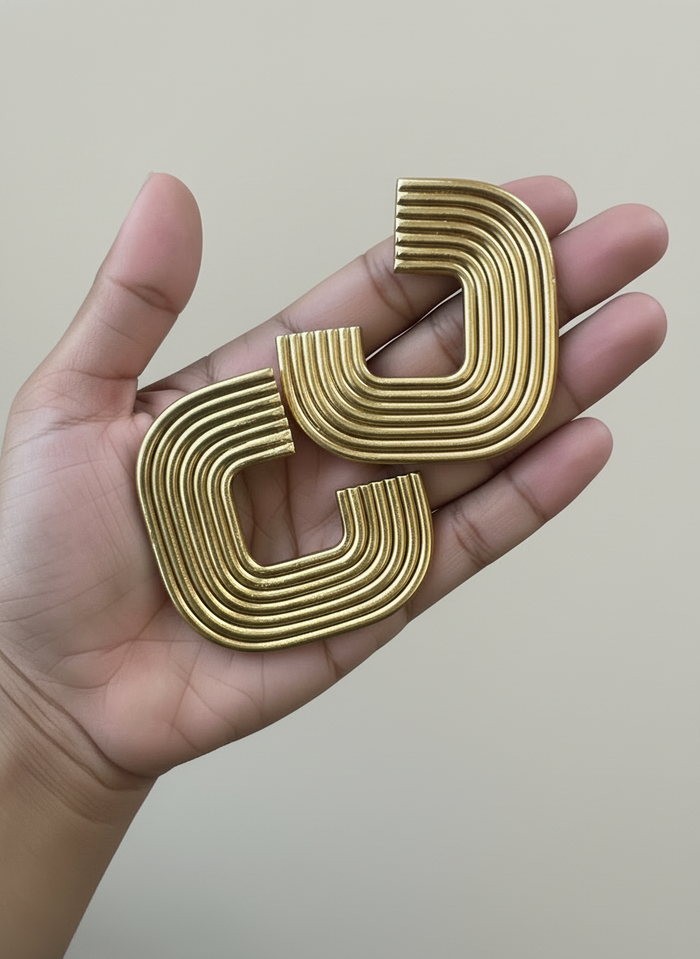 Hand holding the a pair of gold Gia Statement Earrings, handmade by Sunni Dineen.