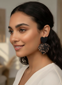 Woman wearing black Lace Puffy Heart Statement Earrings, handmade by Sunni Dineen, with a blurred indoor background.