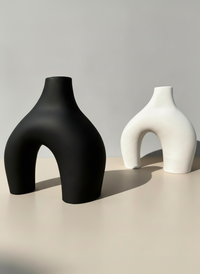 The black and bone-colored Modern Sculptural Horseshoe Vase against a gray background and cream surface.