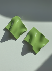 A pair of avocado 'Monae' statement earrings, handmade by Sunni Dineen, on a white surface with shadows and filtered light.