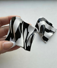 A pair of abstract black & white 'Monae' statement earrings, handmade by Sunni Dineen, on a white surface with shadows and filtered light.