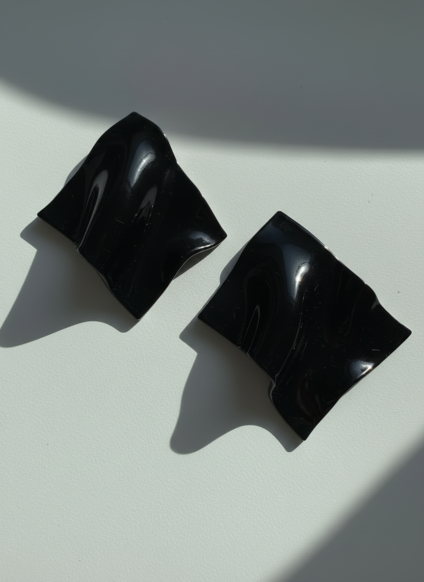 A pair of black 'Monae' statement earrings, handmade by Sunni Dineen, on a white surface with shadows and filtered light.