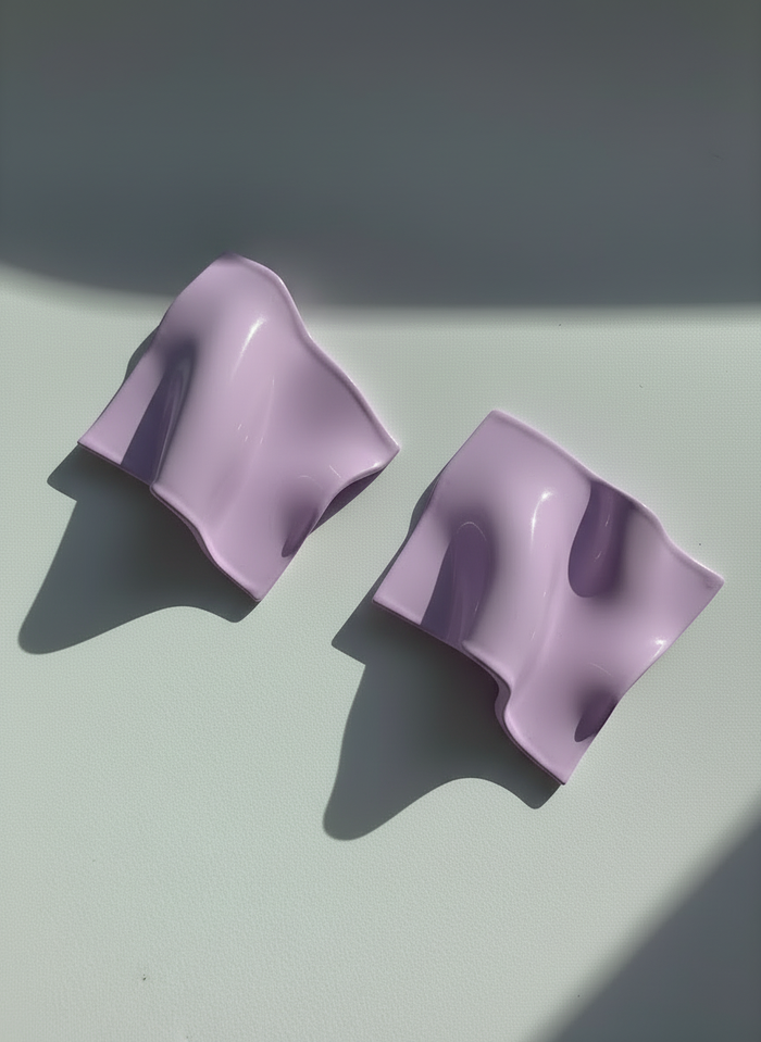 A pair of lavender 'Monae' statement earrings, handmade by Sunni Dineen, on a white surface with shadows and filtered light.