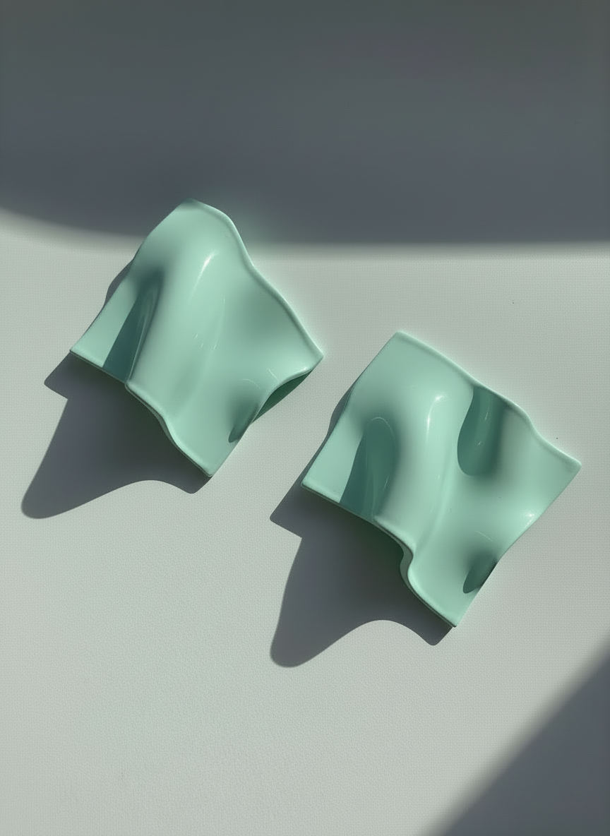 A pair of mint green 'Monae' statement earrings, handmade by Sunni Dineen, on a white surface with shadows and filtered light.