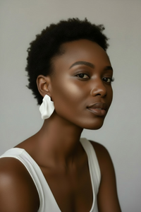 A woman styled wearing white "Monae" sculptural statement earrings and a white bodycon dress.