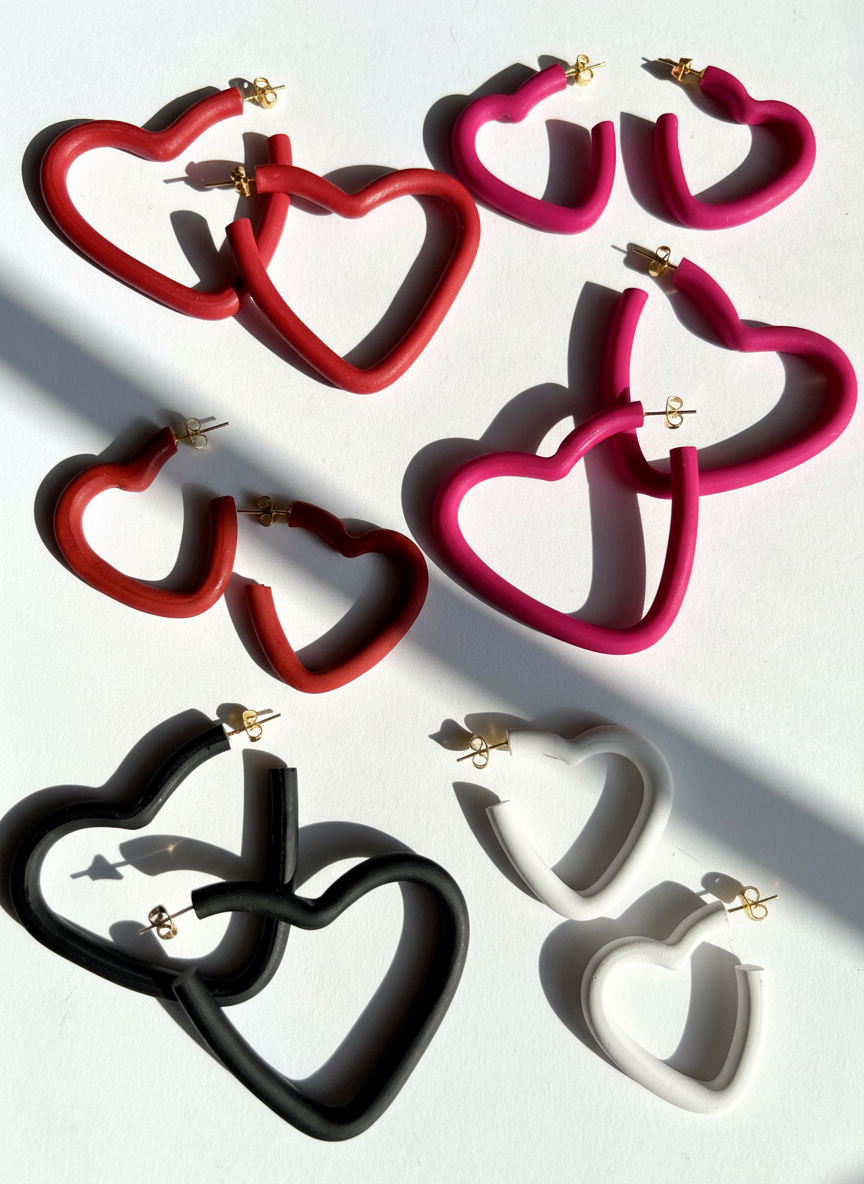Several pairs of open heart hoop earrings in red, pink, black, and white on a white background, handmade by Sunni Dineen.
