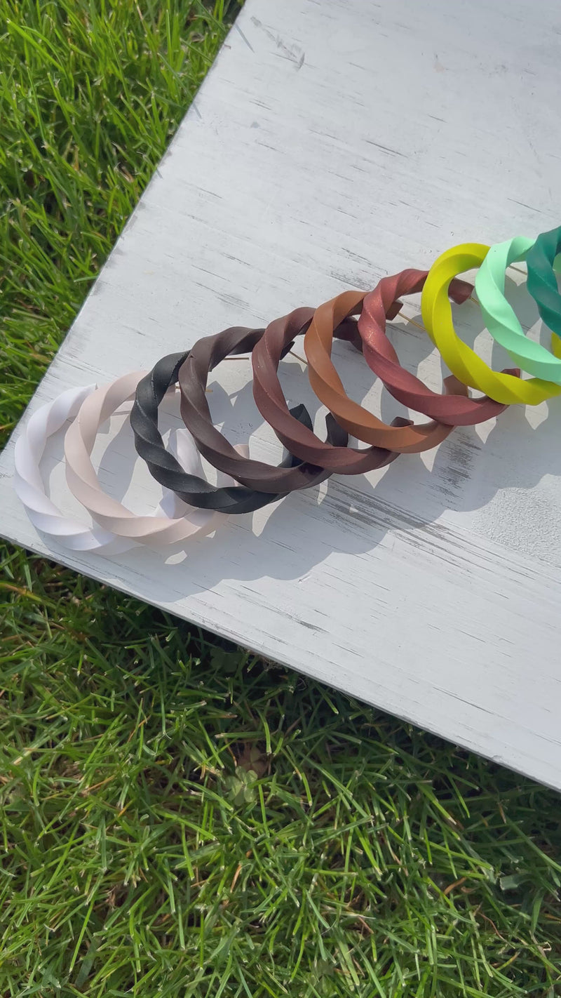 A video of a collection of 'Helix Clay Hoop Earrings' on a white wooden surface surrounded by green grass.