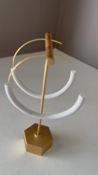 A video of the white 'Weightless Infinity Hoops' on a gold earring stand on a white surface against a gray backgrond.
