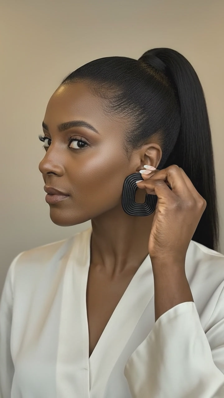 A video of a model wearing a white blouse while donning a pair of black 'Gia' statement earrings handmade by Sunni Dineen, against a beige background.