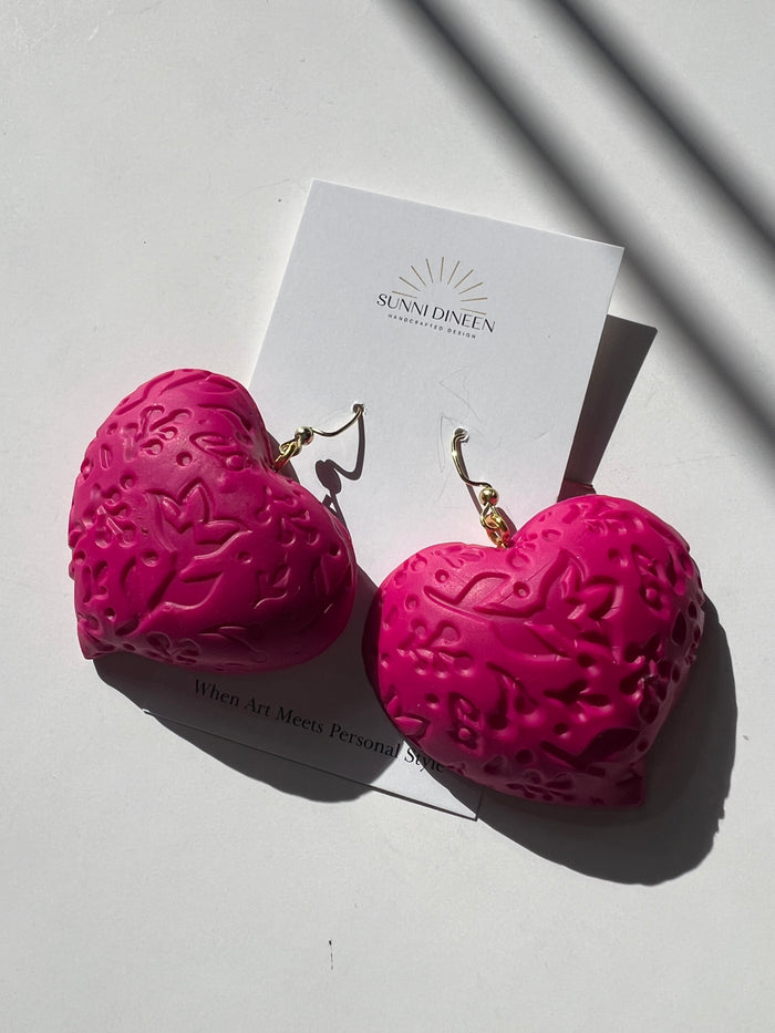The Puffy Heart Statement Earrings in fuchsia, displayed on a white earring card on a white surface, handmade by Sunni Dineen.