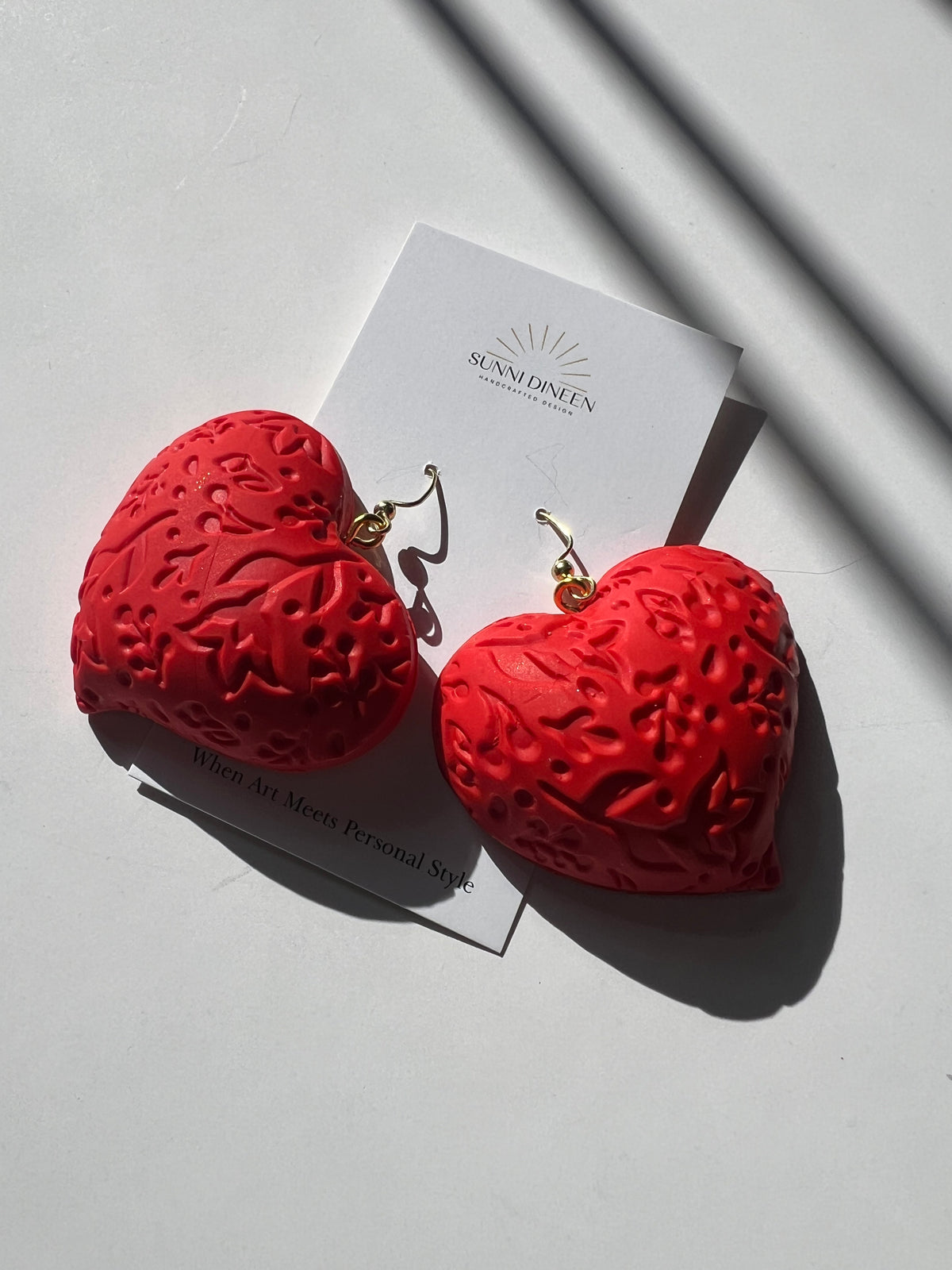 The Puffy Heart Statement Earrings in red, displayed on a white earring card on a white surface, handmade by Sunni Dineen.