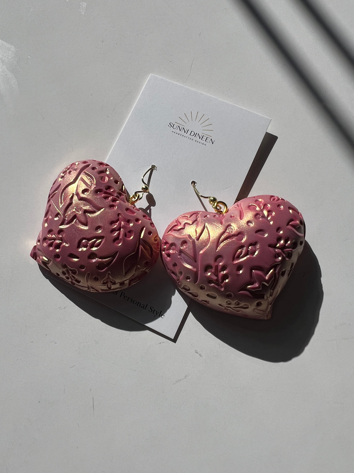 The Puffy Heart Statement Earrings in rose-gold, displayed on a white earring card on a white surface, handmade by Sunni Dineen.
